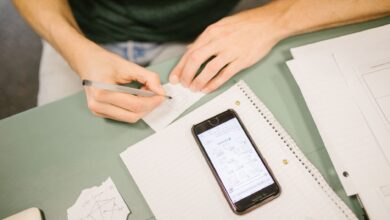 Close-up of student writing notes with a phone displaying diagrams. Concept of study aids and education.