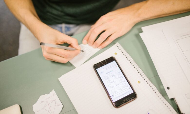 Close-up of student writing notes with a phone displaying diagrams. Concept of study aids and education.