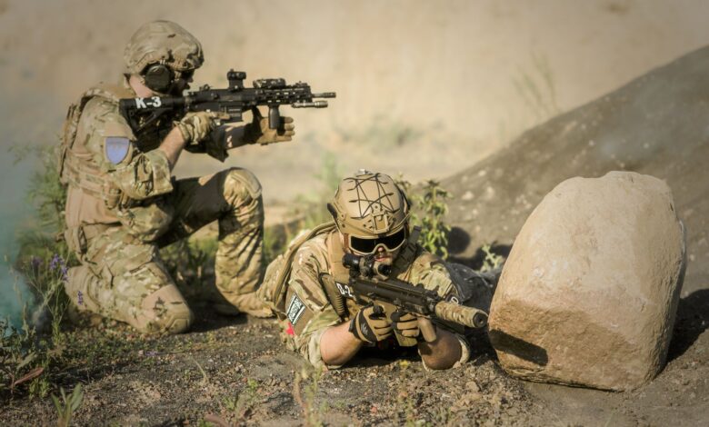 Two soldiers in camouflage uniforms practice tactical maneuvers in a desert environment, exhibiting teamwork and precision.