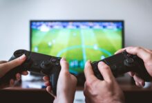 Close-up of hands holding gaming controllers in front of a TV. Engaged in a video gaming session.