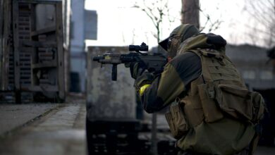 A soldier in camouflage with a rifle prepares in an urban environment, ready for action.