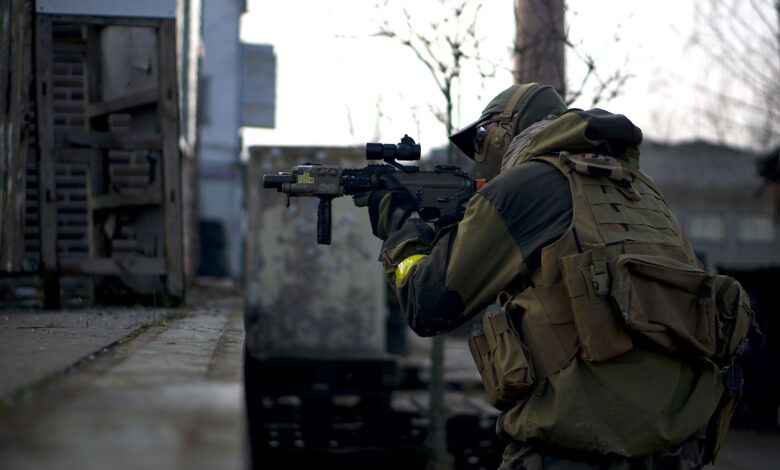 A soldier in camouflage with a rifle prepares in an urban environment, ready for action.