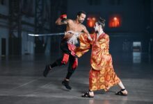 A dynamic martial arts cosplay scene featuring a kimono-clad fighter and a tattooed fighter in motion, indoors.