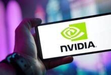 Close-up of a hand holding a smartphone showing the NVIDIA logo on screen with a blurred background.