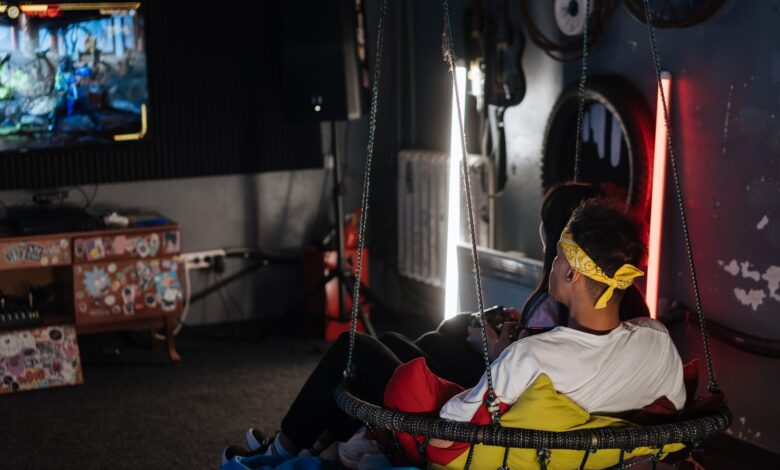 Two friends gaming indoors on a comfy swing chair, enjoying leisure time.