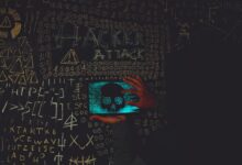A hacker in a black hoodie using a tablet displaying a skull, surrounded by chalk symbols and 'Hacker Attack' text.