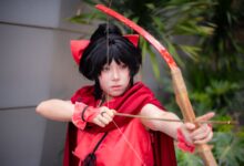Young cosplayer dressed as an archer in a red costume poses outdoors.