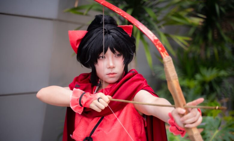 Young cosplayer dressed as an archer in a red costume poses outdoors.