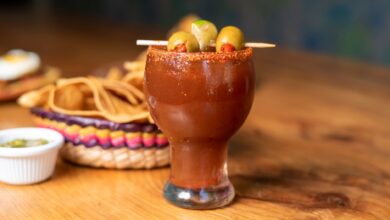 Chilled Mexican michelada garnished with olives and served alongside nachos on a wooden table.