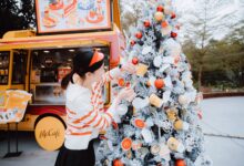 Woman decorating a McDonald's themed Christmas tree outside a McCafe truck during winter festivities.
