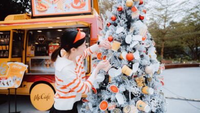 Woman decorating a McDonald's themed Christmas tree outside a McCafe truck during winter festivities.