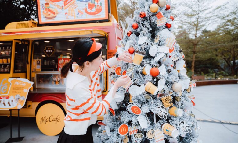 Woman decorating a McDonald's themed Christmas tree outside a McCafe truck during winter festivities.