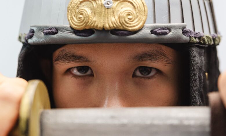 Close-up of a samurai warrior's eyes with a traditional helmet, holding a sword.