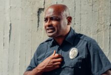 Portrait of a police officer in uniform with a badge, standing outdoors in natural light.