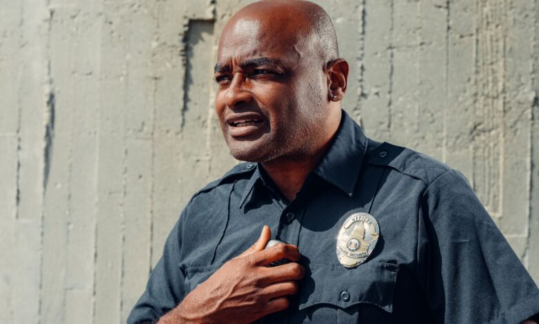 Portrait of a police officer in uniform with a badge, standing outdoors in natural light.