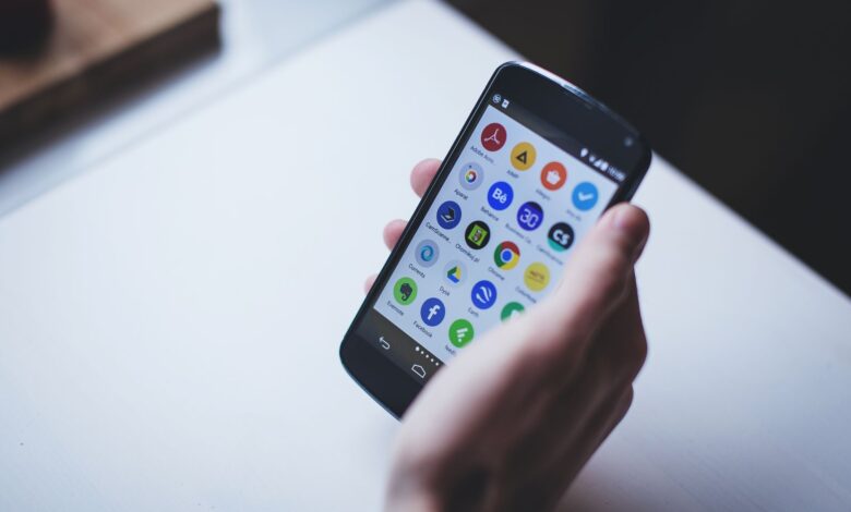 Close-up of a person holding a smartphone with various app icons visible on the screen.