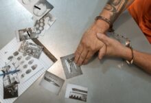 A handcuffed individual examines evidence photos and documents during an investigation.