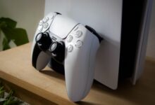 Close-up of PlayStation 5 with DualSense controller on a wooden shelf.