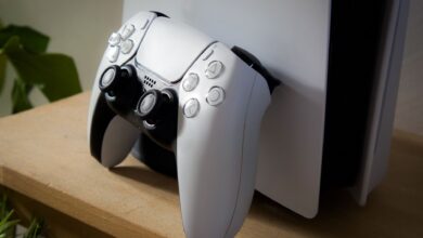 Close-up of PlayStation 5 with DualSense controller on a wooden shelf.