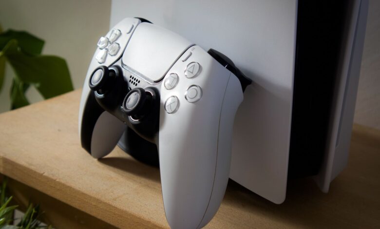 Close-up of PlayStation 5 with DualSense controller on a wooden shelf.