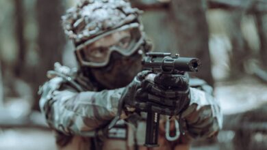 A focused soldier in tactical gear aiming a handgun in a forest setting.