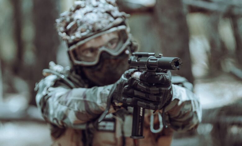 A focused soldier in tactical gear aiming a handgun in a forest setting.