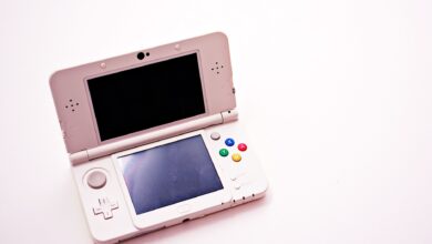 A clean shot of a white portable gaming console with two screens.