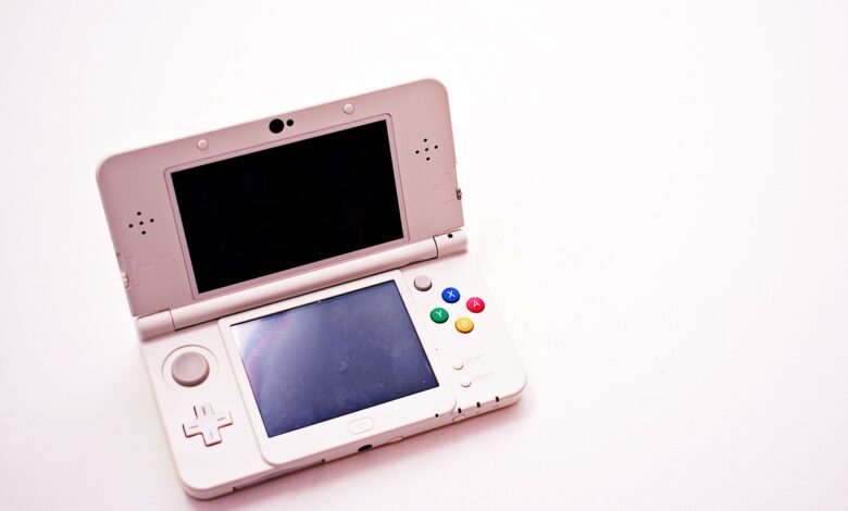 A clean shot of a white portable gaming console with two screens.