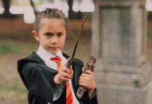 A young boy in a wizard costume holding a wand and book in an outdoor setting.