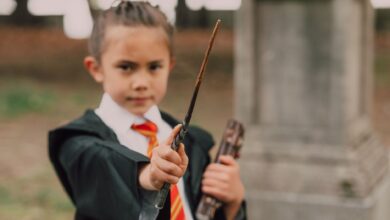 A young boy in a wizard costume holding a wand and book in an outdoor setting.