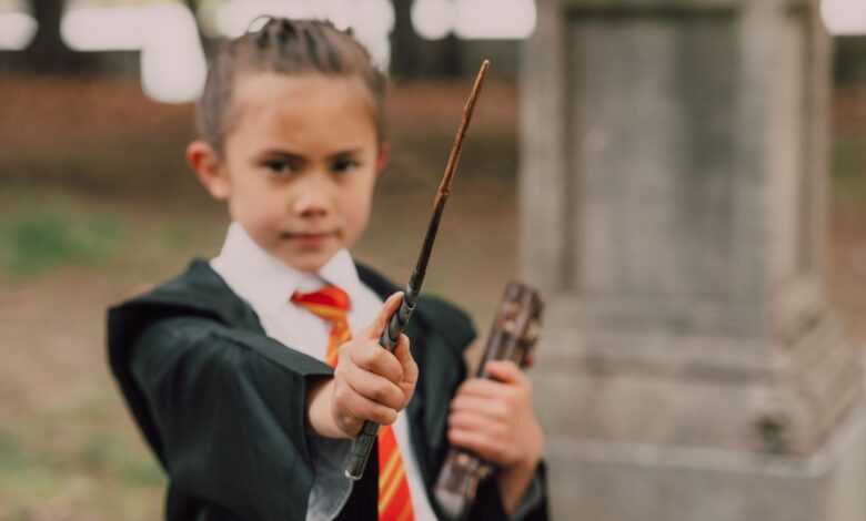 A young boy in a wizard costume holding a wand and book in an outdoor setting.