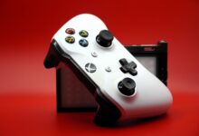 Close-up of a white gaming controller with black buttons against a vivid red backdrop.