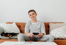 Teenager playing video games on the sofa with a dog sleeping beside him.