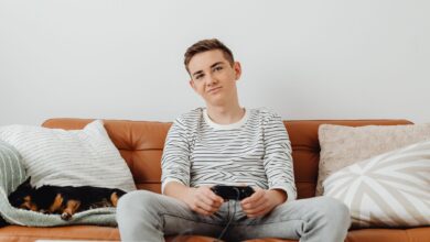 Teenager playing video games on the sofa with a dog sleeping beside him.