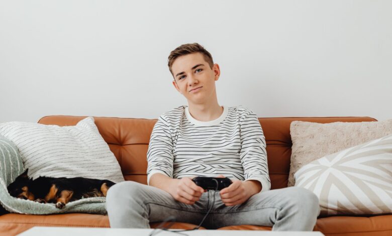 Teenager playing video games on the sofa with a dog sleeping beside him.