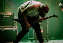 A dynamic guitarist bends forward in a passionate performance on stage with electric guitar and amplifiers.