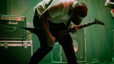 A dynamic guitarist bends forward in a passionate performance on stage with electric guitar and amplifiers.