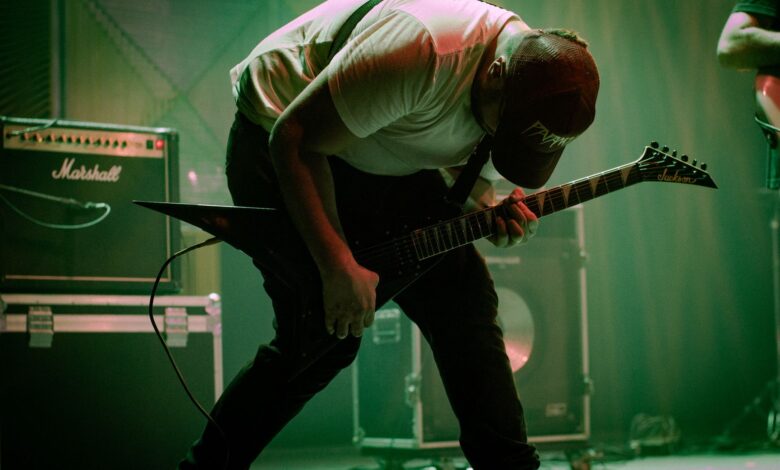 A dynamic guitarist bends forward in a passionate performance on stage with electric guitar and amplifiers.