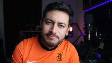 Close-up portrait of a man in an orange jersey next to a microphone in a cozy indoor studio.