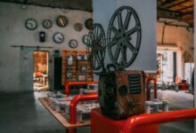 Rustic vintage film projector in an industrial-themed room with wall clocks.
