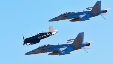 Jet fighters fly in formation with a vintage warplane against a clear blue sky.