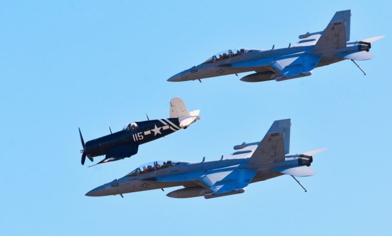 Jet fighters fly in formation with a vintage warplane against a clear blue sky.