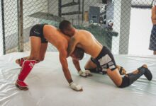 Two men engaged in a Brazilian Jiu-Jitsu grappling match in an indoor gym.