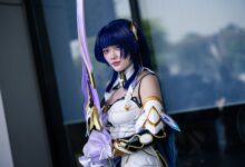 A cosplayer dressed in detailed futuristic armor wielding a long sword outdoors.