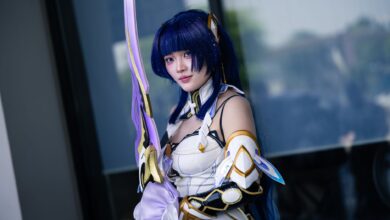 A cosplayer dressed in detailed futuristic armor wielding a long sword outdoors.