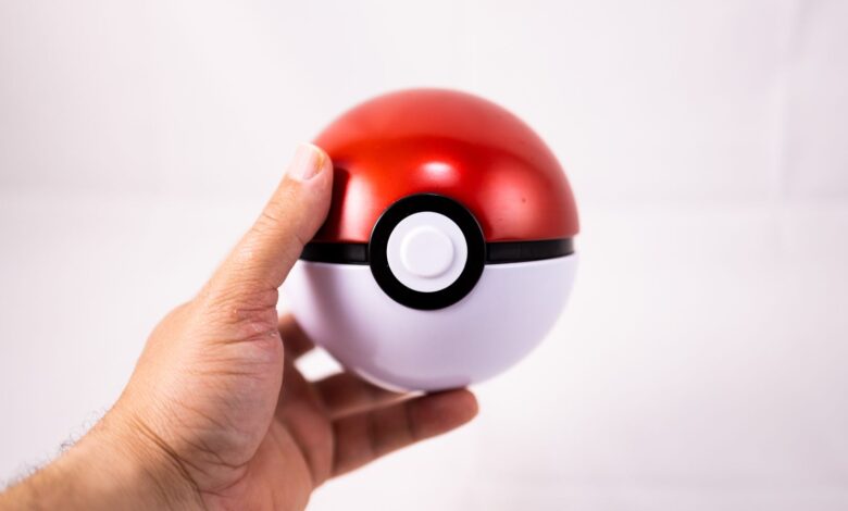Close-up of a human hand holding a red Pokeball toy against a white background.