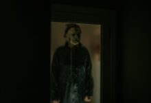 A chilling figure in a Halloween mask is reflected in a dark window, creating an eerie atmosphere.