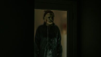 A chilling figure in a Halloween mask is reflected in a dark window, creating an eerie atmosphere.
