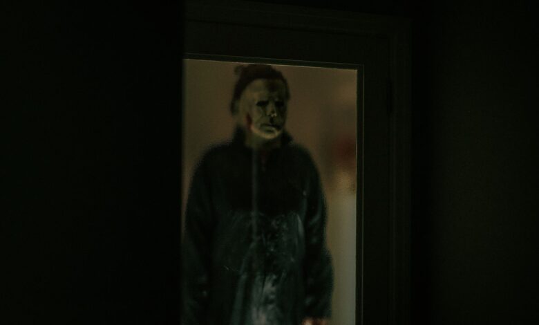 A chilling figure in a Halloween mask is reflected in a dark window, creating an eerie atmosphere.