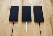 Three smartphones connected to chargers on a wooden surface, showcasing modern technology